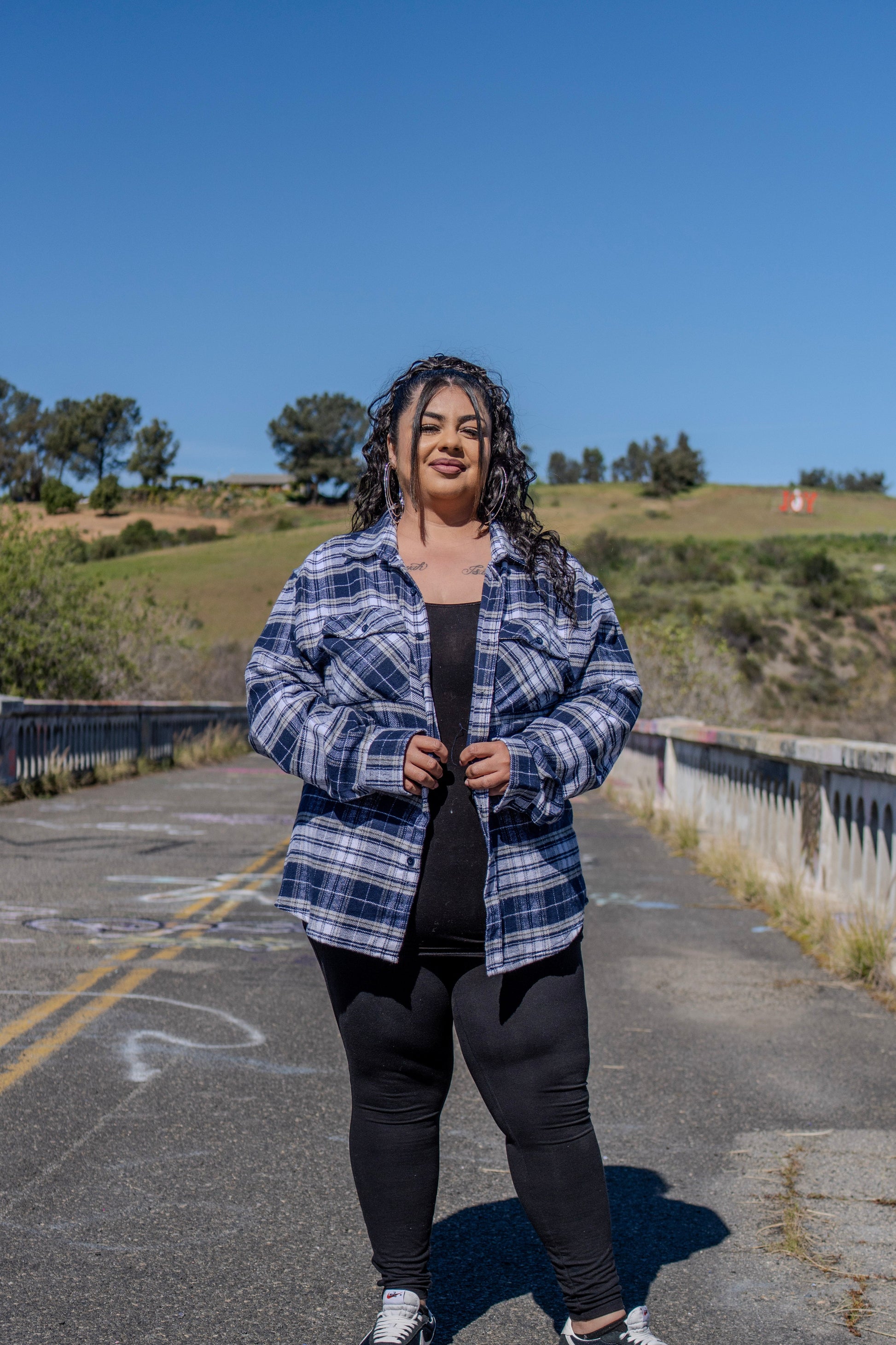 Person standing on a road with a blue sky and greenery in the background