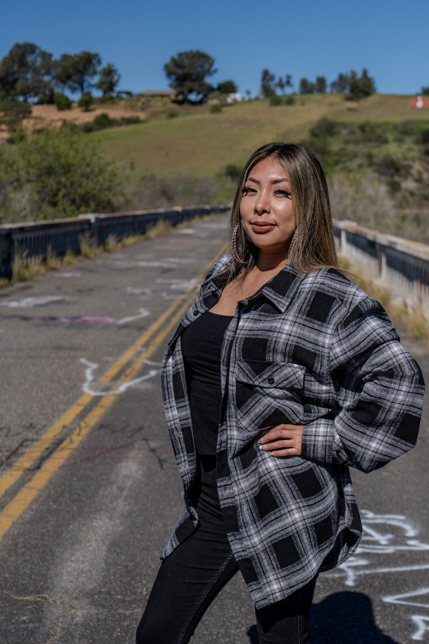 Woman in a plaid jacket standing on an empty road with greenery in the background